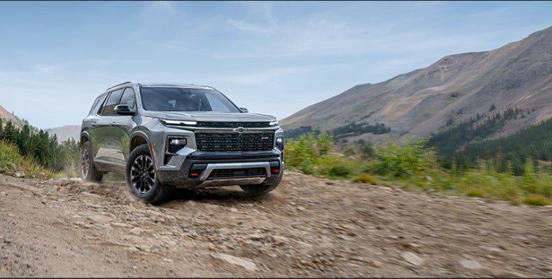 Chevrolet Traverse SUV driving on a rugged mountain road surrounded by scenic hills.